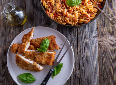 Italian pasta dish with breaded chicken breast served with fusilli noodles in a delicious tomato, basil sauce on wooden table. Overhead viewの写真素材