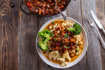 Healthy goulash with pasta and vegetable. Low fat meat dish. Cooked with turkey breast and served on a plate and skillet isolated on wooden table. Closeup and top viewの写真素材
