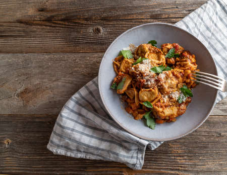 Vegetarian pasta dish with tomtoes, vegetables and parmesan cheese. Served in a bowl or plate on wooden table background. Side view with copy spaceの写真素材