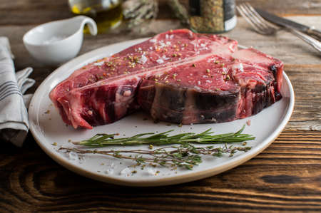 Organic and grass fed t-bone or porterhouse steak with salt and pepper seasoning served raw and uncooked on wooden table backgroundの写真素材