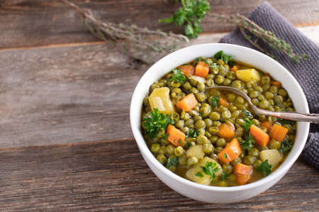 Vegetarian, vegan and gluten free stew with green peas, potatoes and vegetables. Served in a bowl with spoon on rustic and wooden table with copy spaceの写真素材