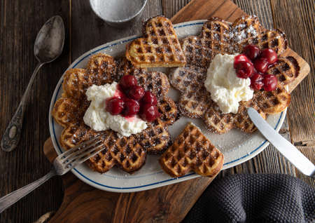 Waffles with cherries and whipped cream. Traditional homemade german dessert. Served on a plate on old fashioned and rustic, wooden table background from above closeupの写真素材