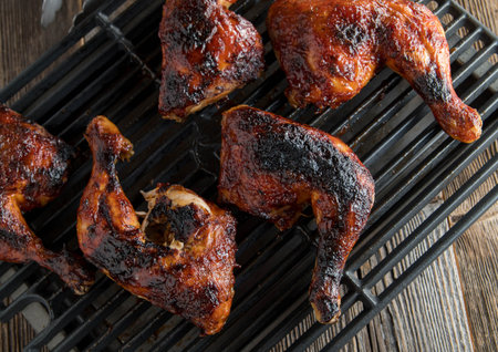 Grilled chicken legs on a grill grate. Fresh grilled marinated and honey glazed chicken legs. Served...