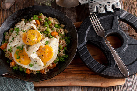 Fitness meal with fried eggs, brown rice and vegetables. Served in a rustic frying pan with dumbbell on wooden table background from aboveの写真素材