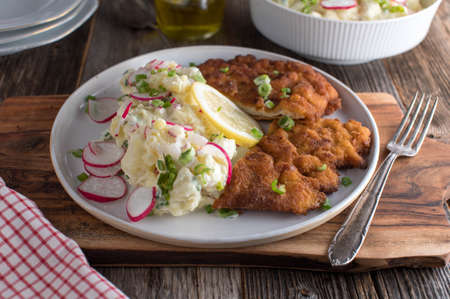 Schnitzel with potato salad. Traditional german, bavarian dish fresh and homemade cooked. Served on a plate with lemon on rustic and wooden table background. Ready to eatの写真素材