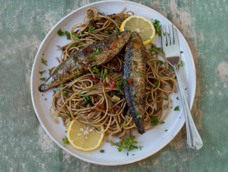 Pan fried sardines with pasta cooked with olive oil, garlic, peppers and parsley on a plateの写真素材