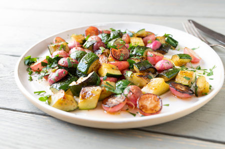 Pan fried caramelized vegetables with red radish, zucchini, parsley and olive oil on a plateの写真素材