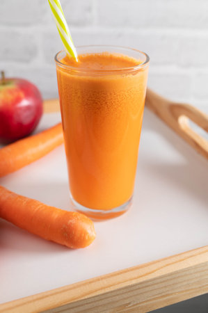 Breakfast juice freshly squeezed with carrots and apples in a drinking glass with straw.の写真素材