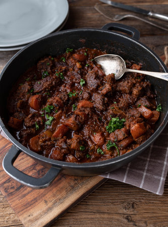 Braised pork with carrots and gravy in a pot on wooden tableの写真素材