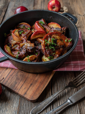 Pork chops with braised apples and onions in a pot on wooden tableの写真素材