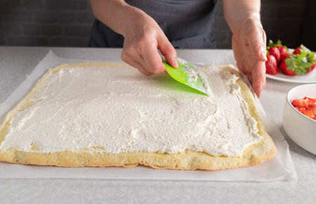Whipped cream is spread on a sponge cake for making swiss roll