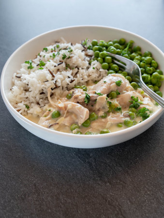 Chicken fricassee or ragout with basmati rice and wild rice. Served with green peas on a plate isolated on a tableの写真素材