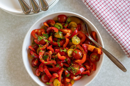 Salad with peppers, red and yellow cherry tomatoes in a bowl with spoonの写真素材