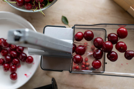 Sour cherries being processed in a cherry pitter on a marble countertop
