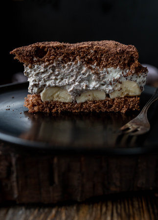 Tiramisu cake with whipped cream and banana on a black plateの写真素材