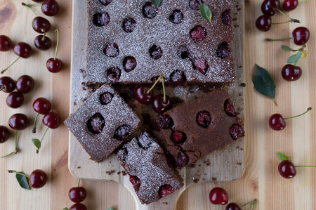 Chocolate brownies with cherries and powdered sugar on a wooden boardの写真素材