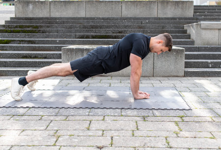 Young man doing a triangle push-up or diamond push-up outdoors on an exercise mat on concrete...