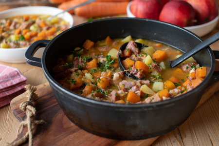 Stew with carrots, potatoes and smoked pork meat in a pot on wooden tableの写真素材