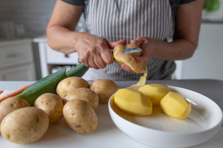 Woman peeling potatoes with a knife in the kitchen. Selective focus.の写真素材