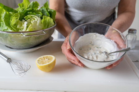 Female hands holding a bowl of salad dressing with sour cream and lemon.の写真素材