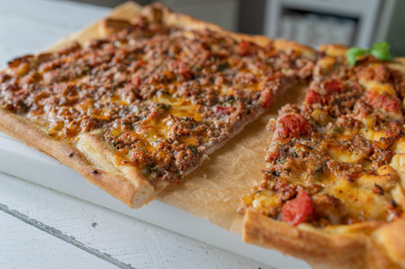 Homemade sliced minced meat pizza with tomatoes, onions and mozzarella cheese on kitchen counterの写真素材