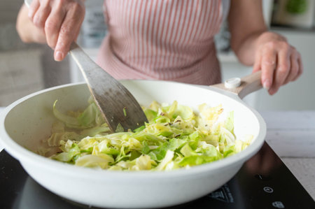 Close-up of a woman frying cabbage in a frying pan in the kitchenの写真素材