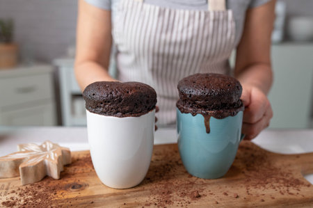 Fresh baked microwave mug cakes served by a woman with apron in the kitchen on kitchen counter....