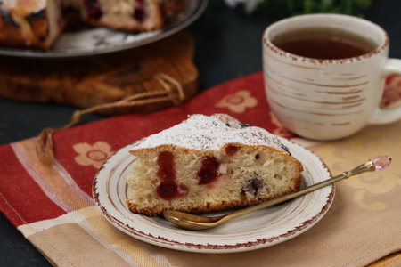 Berry pie with cherries is located on a plate on a dark background. In the foreground is a piece of...