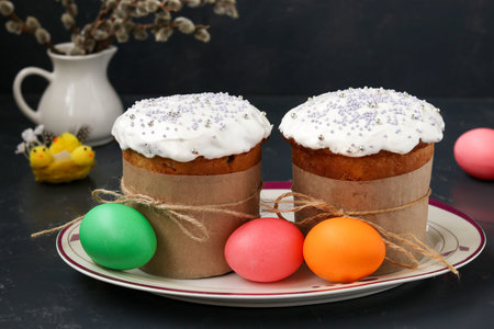 Easter cakes and colorful eggs are located on a plate against a dark background