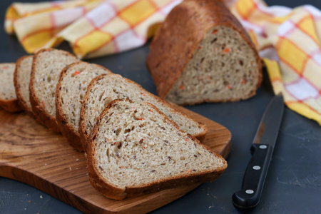 Whole grain carrot bread with flax seeds, located on a wooden board against a dark background