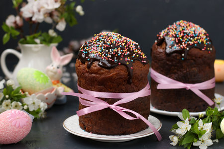 Still life with Easter cakes covered with chocolate icing and colorful eggs on a dark background