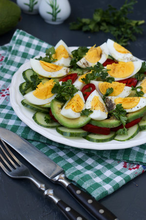 Useful salad of avocado, cucumbers, eggs and sweet pepper located in a plate against a dark...