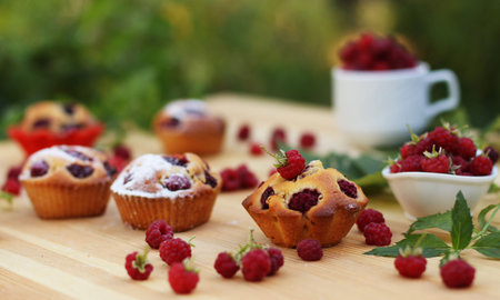Muffins with raspberries are located on a wooden table on the background of green bushes, Around a...