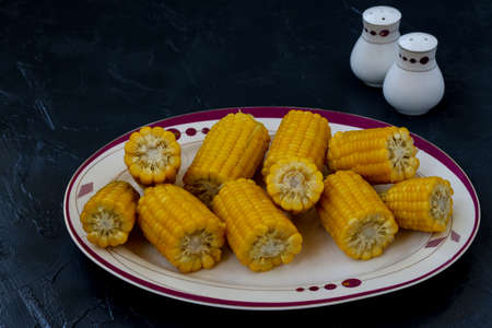 Corn is located on a plate on a dark background with salt and pepper shakers in the backgroundの写真素材