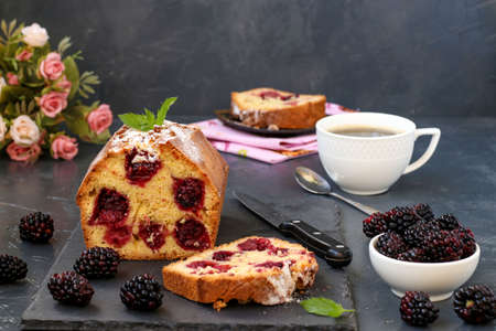 A blackberry muffin is located on a slate plank on a dark background, with a slice of muffin in the foreground, horizontal photoの写真素材