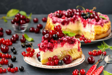 Summer cottage cheese cake with berries is located on a dark background, in the foreground a piece of cake on a plate, horizontal photo, close-upの写真素材