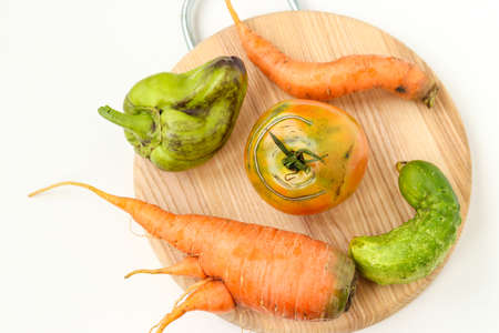 Five ugly vegetables: carrots, cucumber, pepper and tomato on wooden board on white background, ugly food concept, horizontal photo, top viewの写真素材