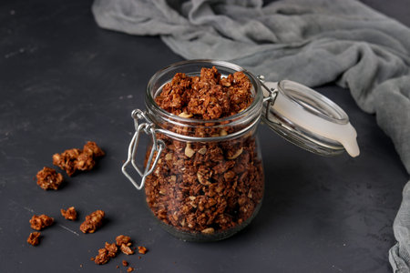 Granola crispy muesli with natural honey, chocolate and nuts in a glass jar against a dark...