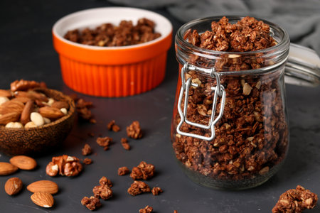 Granola crispy muesli with natural honey, chocolate and nuts in a glass jar against a dark...