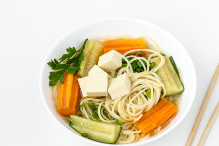 Traditional asian soup with tofu cheese, noodles, carrots and zucchini on white background. This...