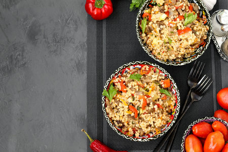 Bulgur with mushrooms and vegetables in a two bowls on a dark background, vegetarian oriental dish,...