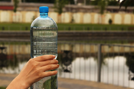 Bottle of mineral water in a female hand in a city park during a morning run, water is a guarantee...