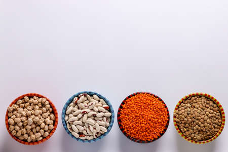 Red and brown lentils, chickpeas and white beans are legumes that contain a lot of protein are located on a white background in bowls, horizontal orientation, copy spaceの写真素材