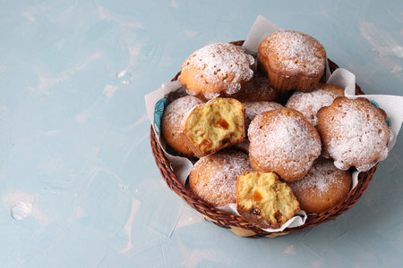 Homemade muffins with dried apricots, sprinkled with powdered sugar in a wicker basket on light blue...