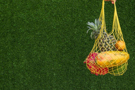 Tropical fruits: mango, papaya, pineapple, dragon and passion fruit in a Yellow Shopping Textile Bag on a green background, horizontal orientationの写真素材