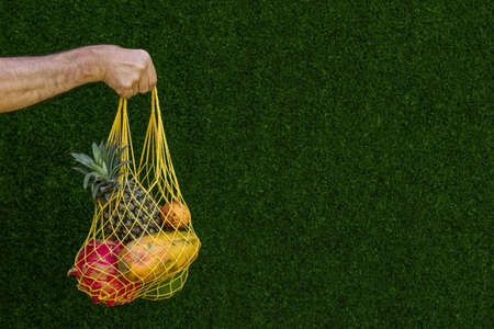 Tropical fruits: mango, papaya, pineapple, dragon and passion fruit in a Yellow Shopping Textile Bag on a green background, horizontal orientation, copy spaceの写真素材