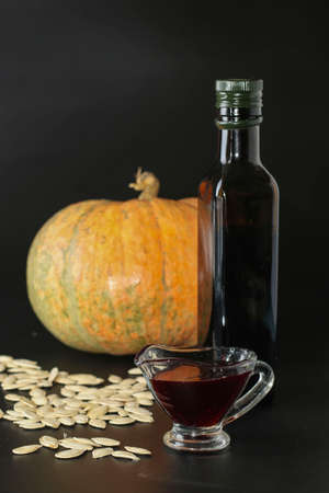 Pumpkin oil in a gravy boat and in a bottle against a dark background, Vertical orientation, Closeupの写真素材