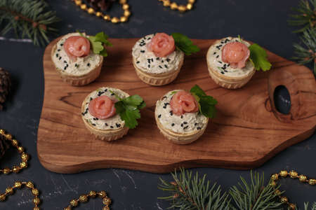 Holiday tartlets with cheese, salmon and avocado on wooden board on dark background, Closeup, horizontal orientationの写真素材