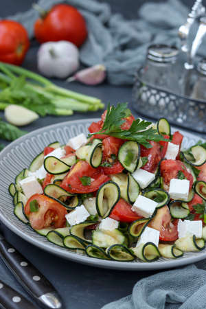 Healthy salad with zucchini, tomatoes and feta, dressed with olive oil in a plate on a dark background, vertical orientation, Closeupの写真素材