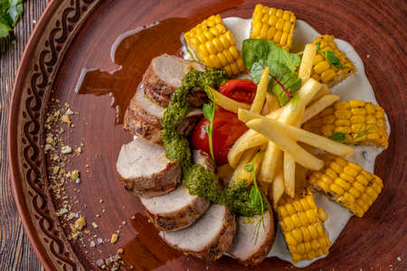 Baked pork served with french fries, corn and pesto, restaurant platter, Horizontal orientation, Closeup, Top viewの写真素材